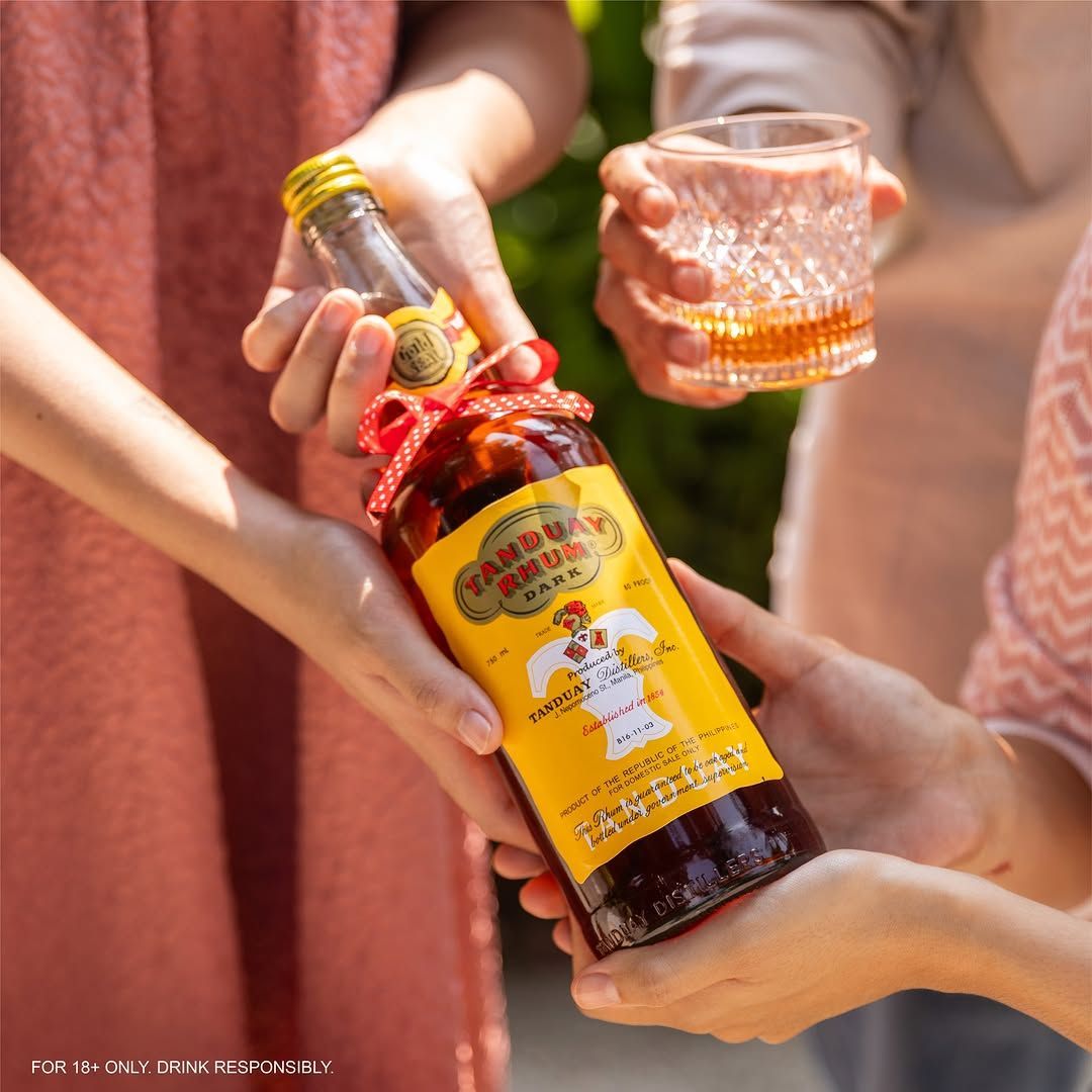 Hands pouring a Tanduay rum bottle into a glass