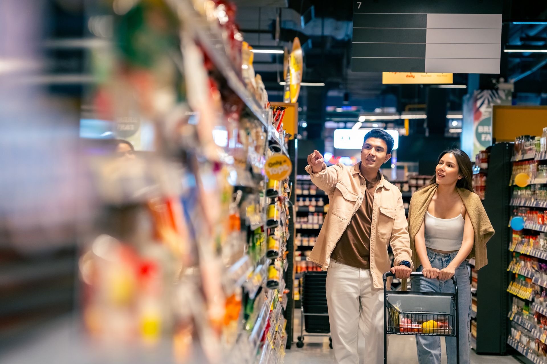 Couple shopping with a cart in a well-stocked grocery store aisle