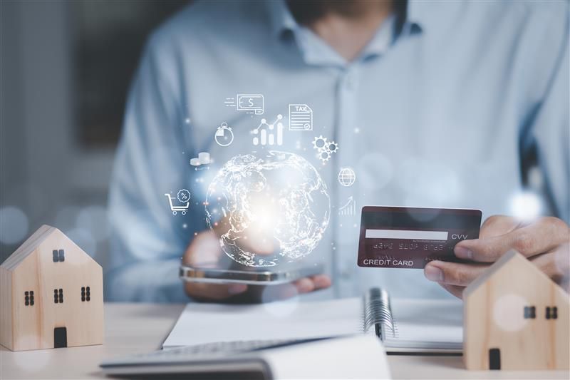 Hand holding a card and phone with digital finance icons and house models