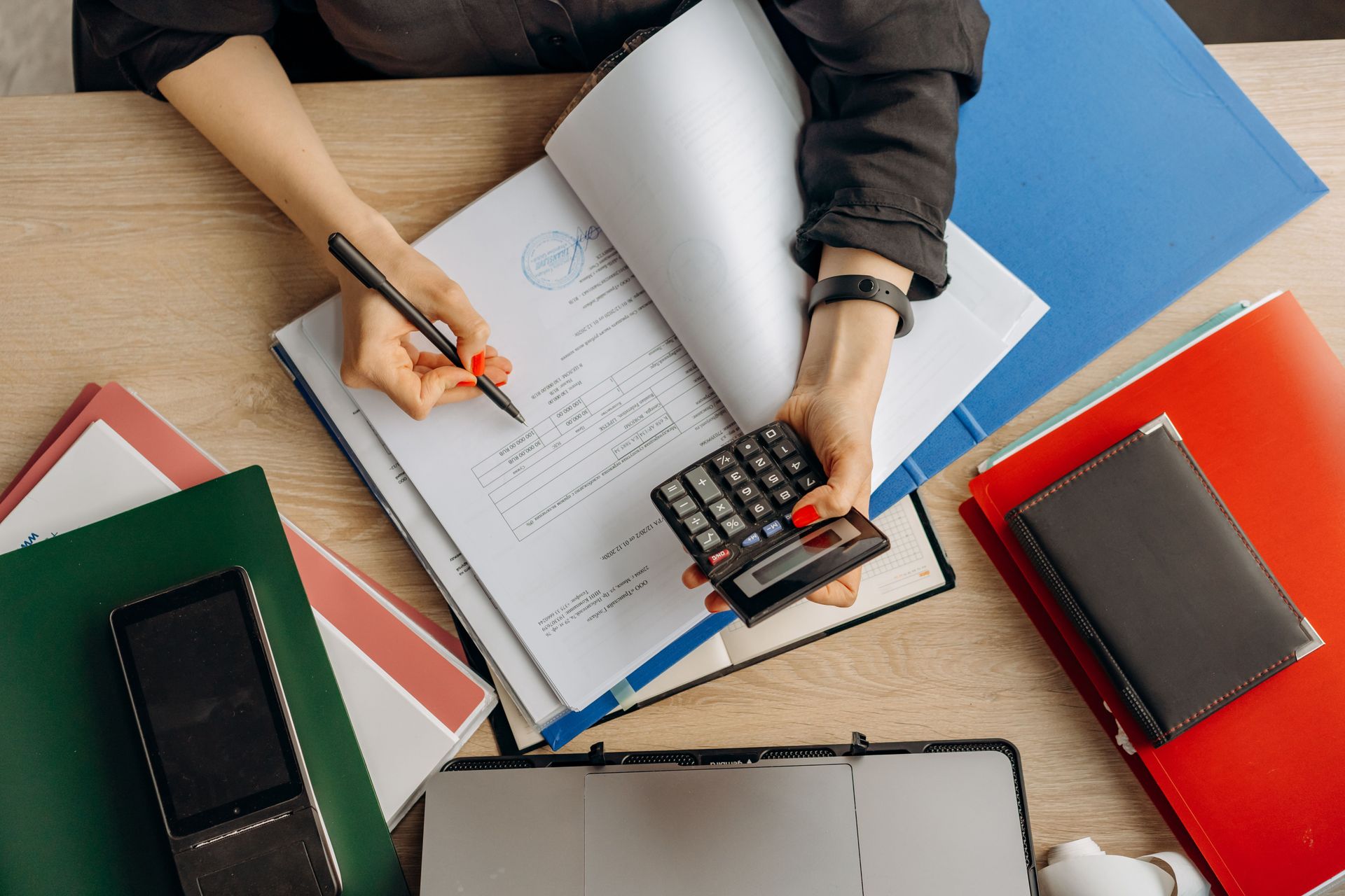 Overhead view of hands using a calculator and notebook at a desk