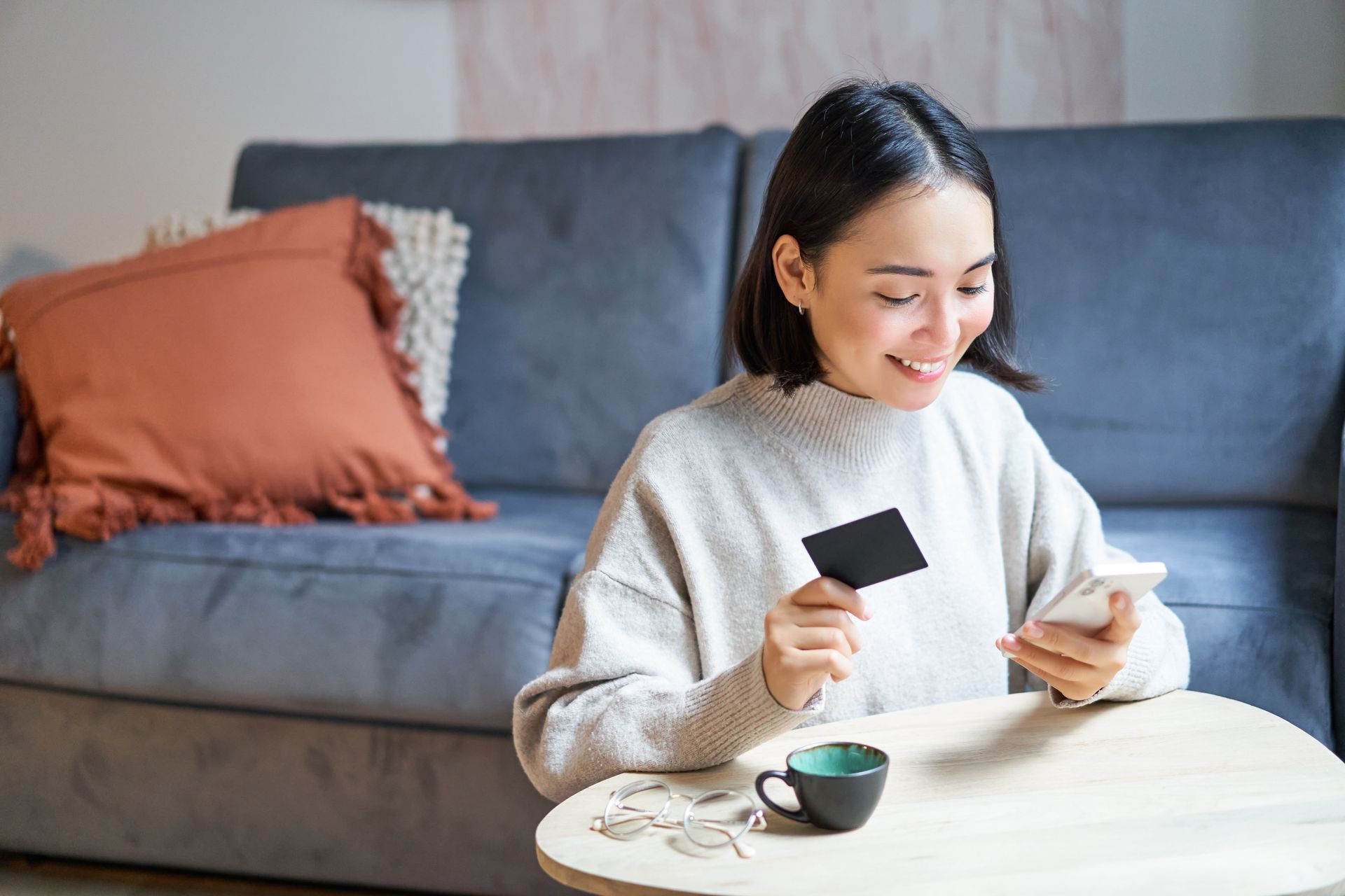 Woman holding a card and phone while relaxing on a sofa with coffee