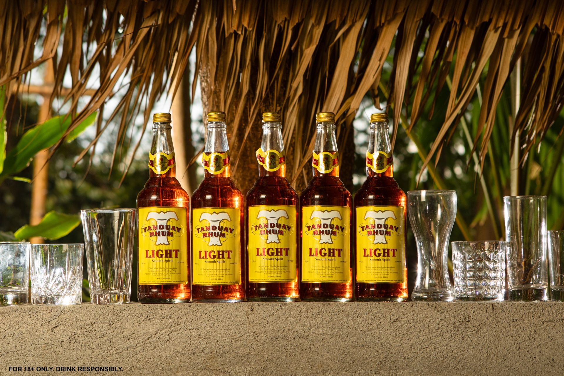 Hands pouring a Tanduay rum bottle into a glass