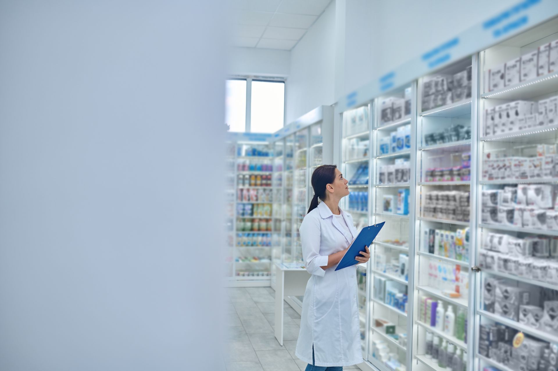 Masked pharmacist holding a medicine bottle and tablet in a pharmacy