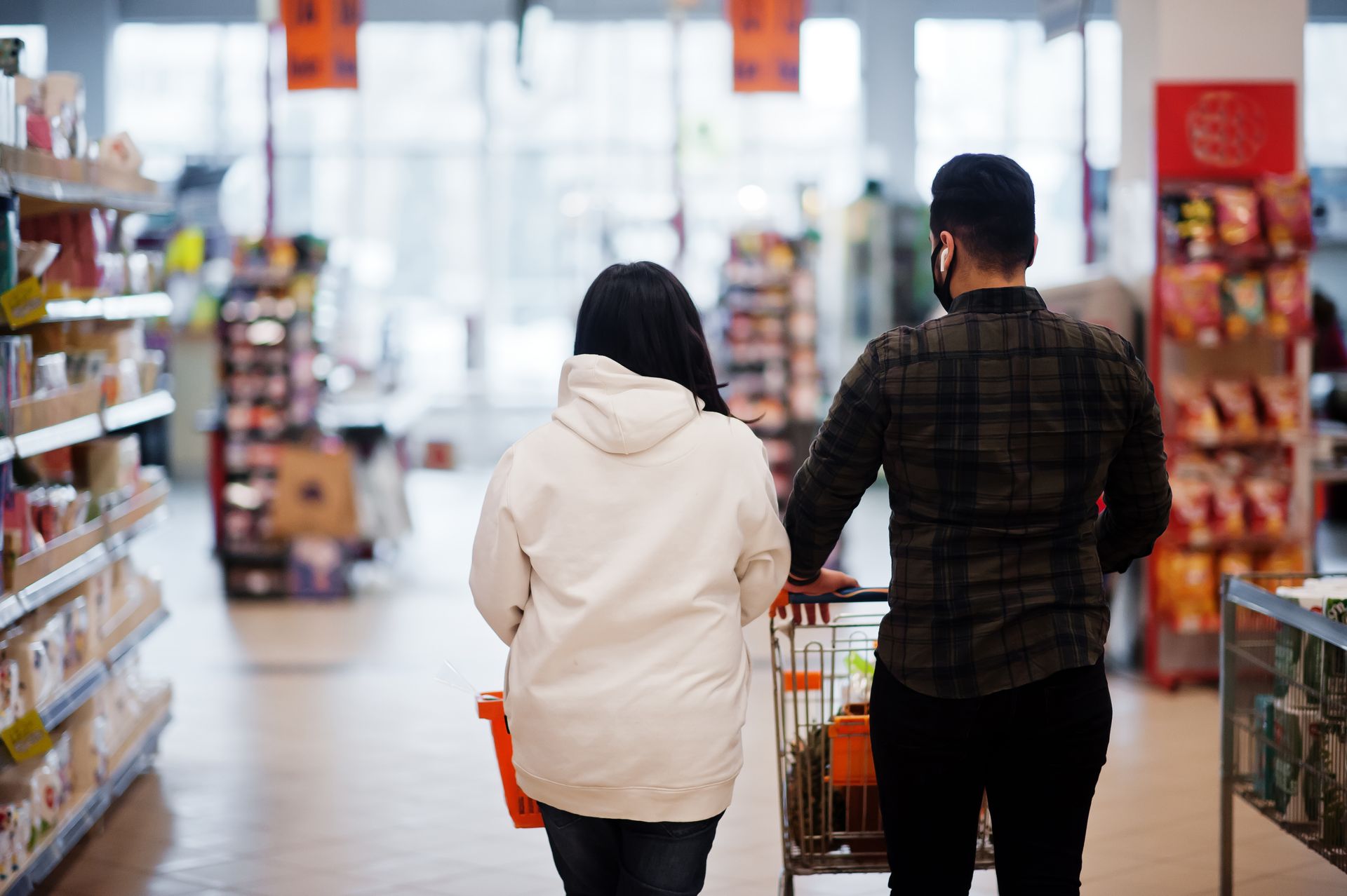 Two women with a shopping basket browsing products in a store aisle