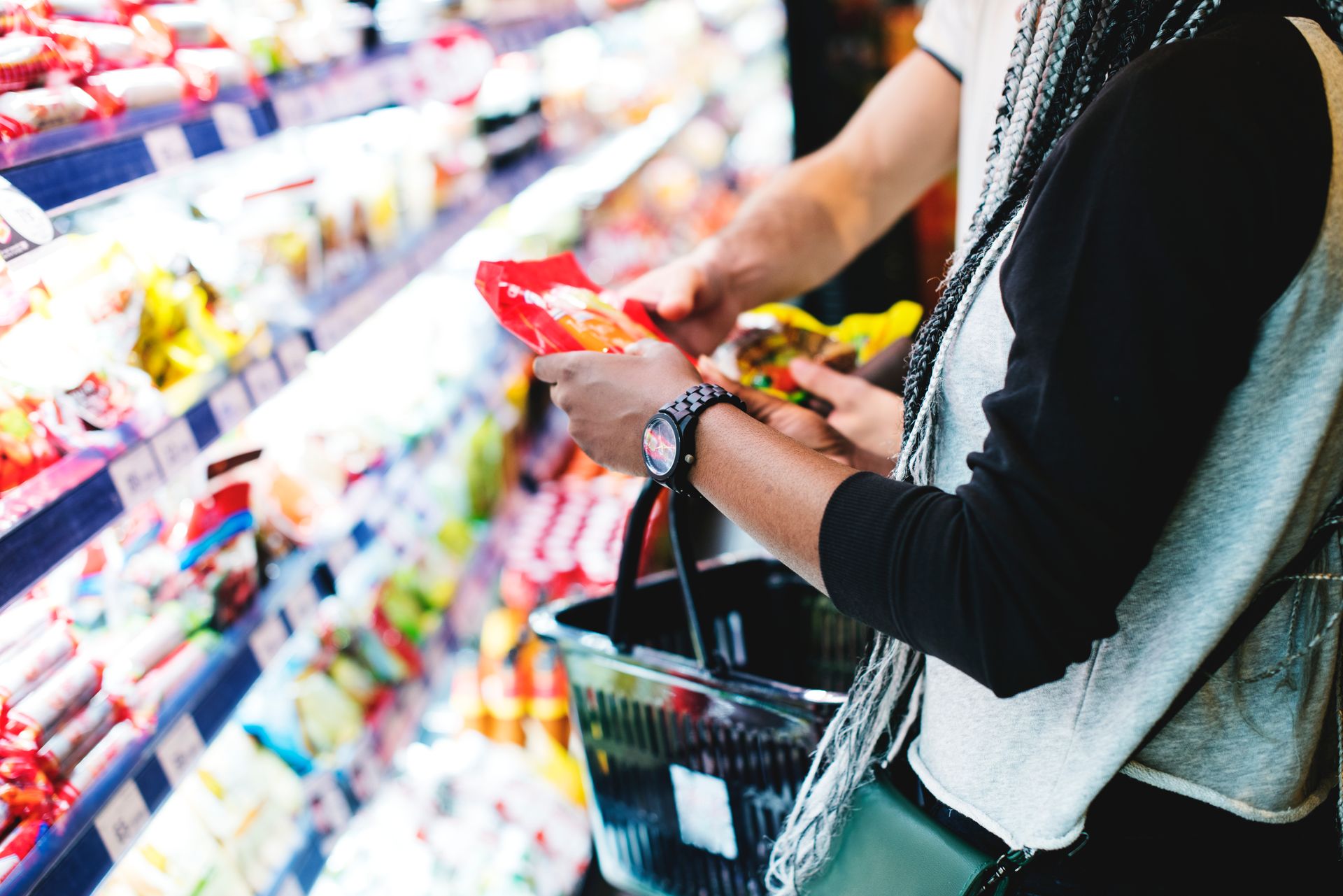 Shopper with a basket selecting products from a supermarket shelf