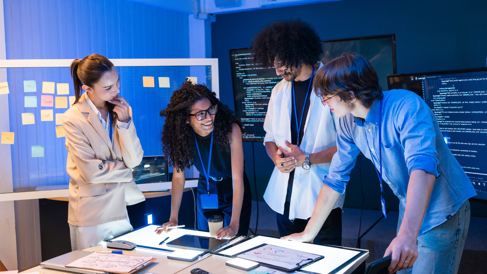 Diverse team collaborating around a table with charts and code screens in a modern office