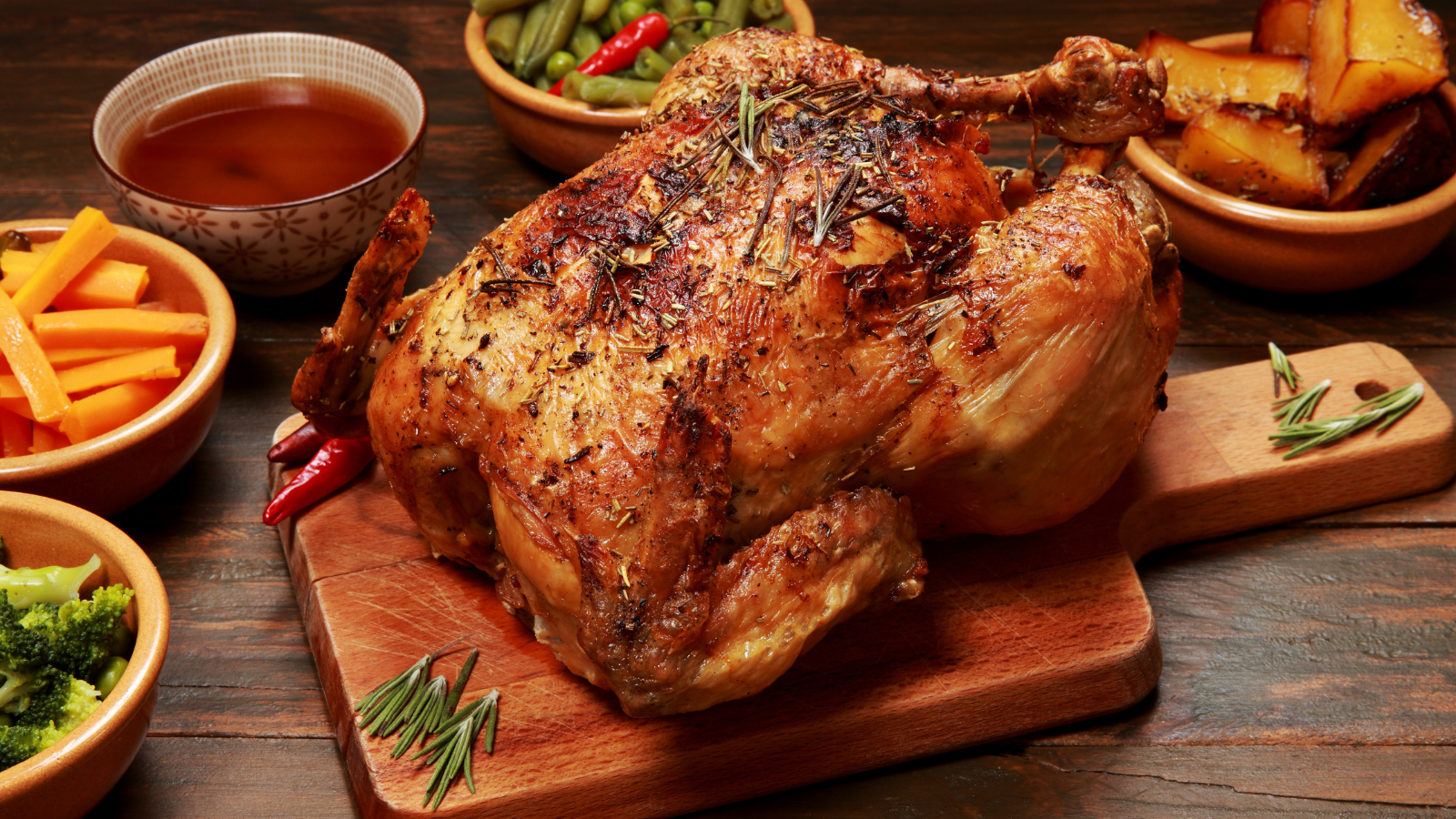 Whole roast chickens on a rotisserie spit turning over an open flame grill
