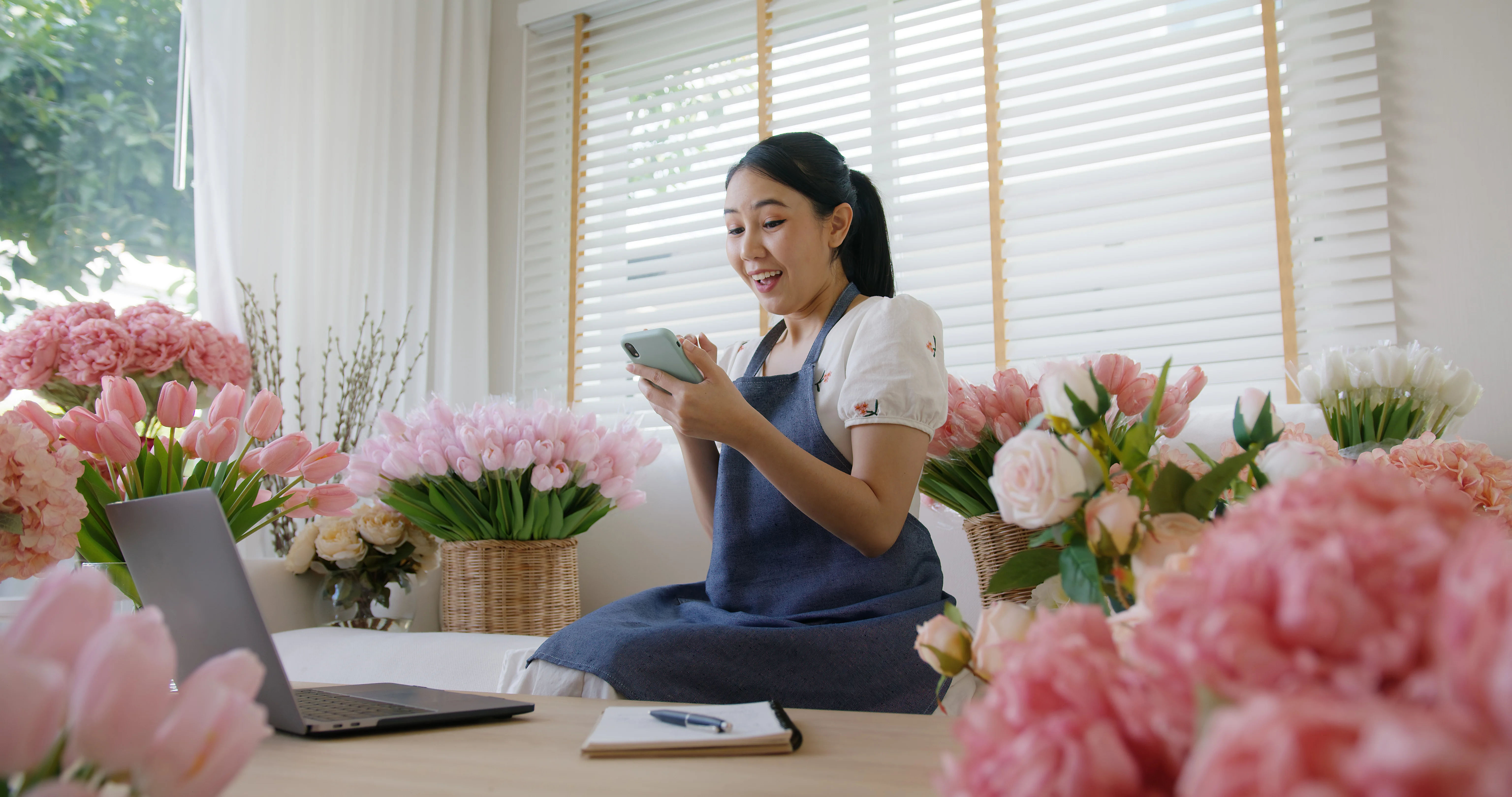 Smiling small business owner checking her phone at a laptop