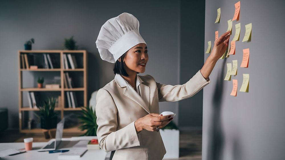 Woman in a chef's hat placing sticky notes on a wall in an office