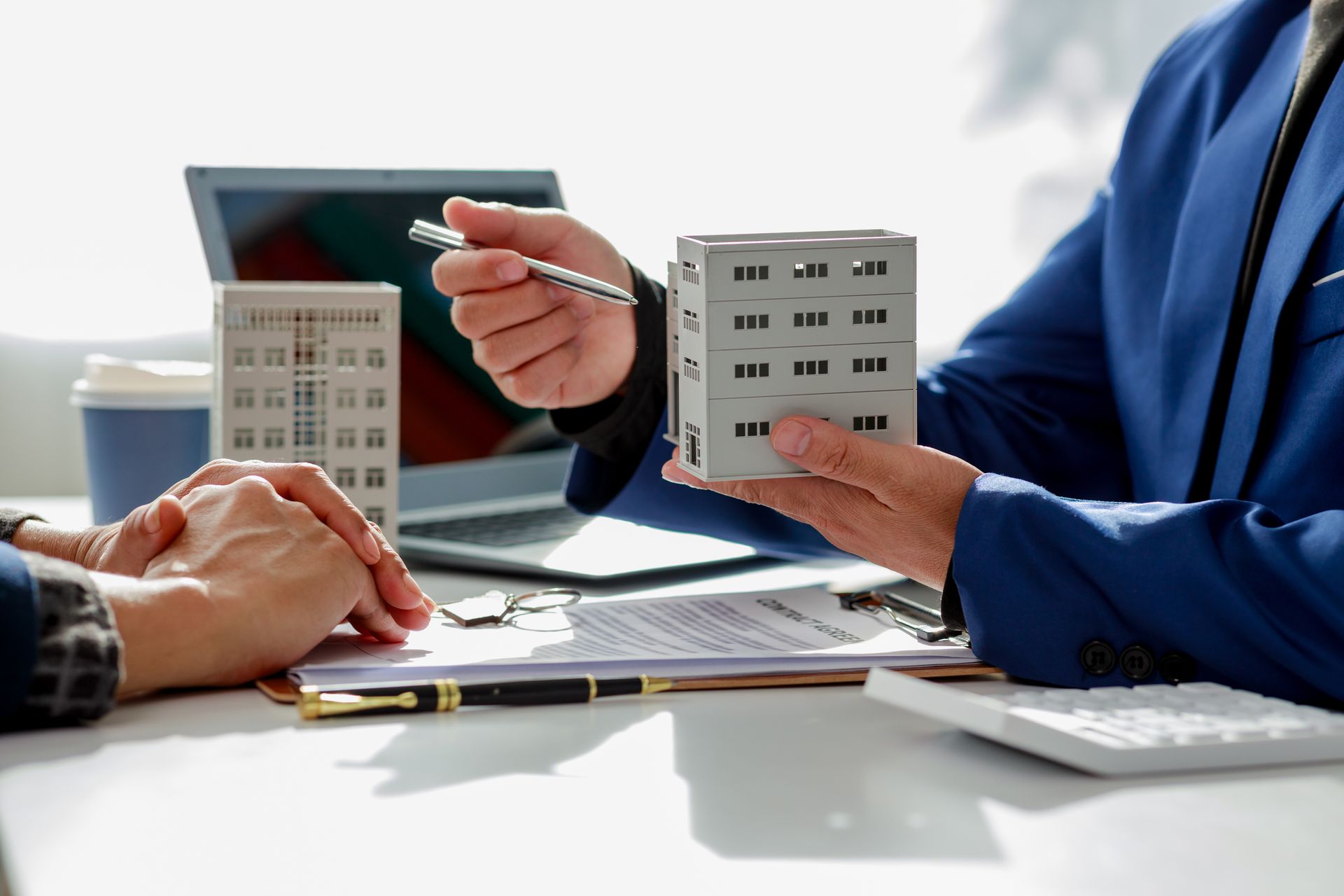 Consultant pointing at a small building model beside a laptop during a meeting