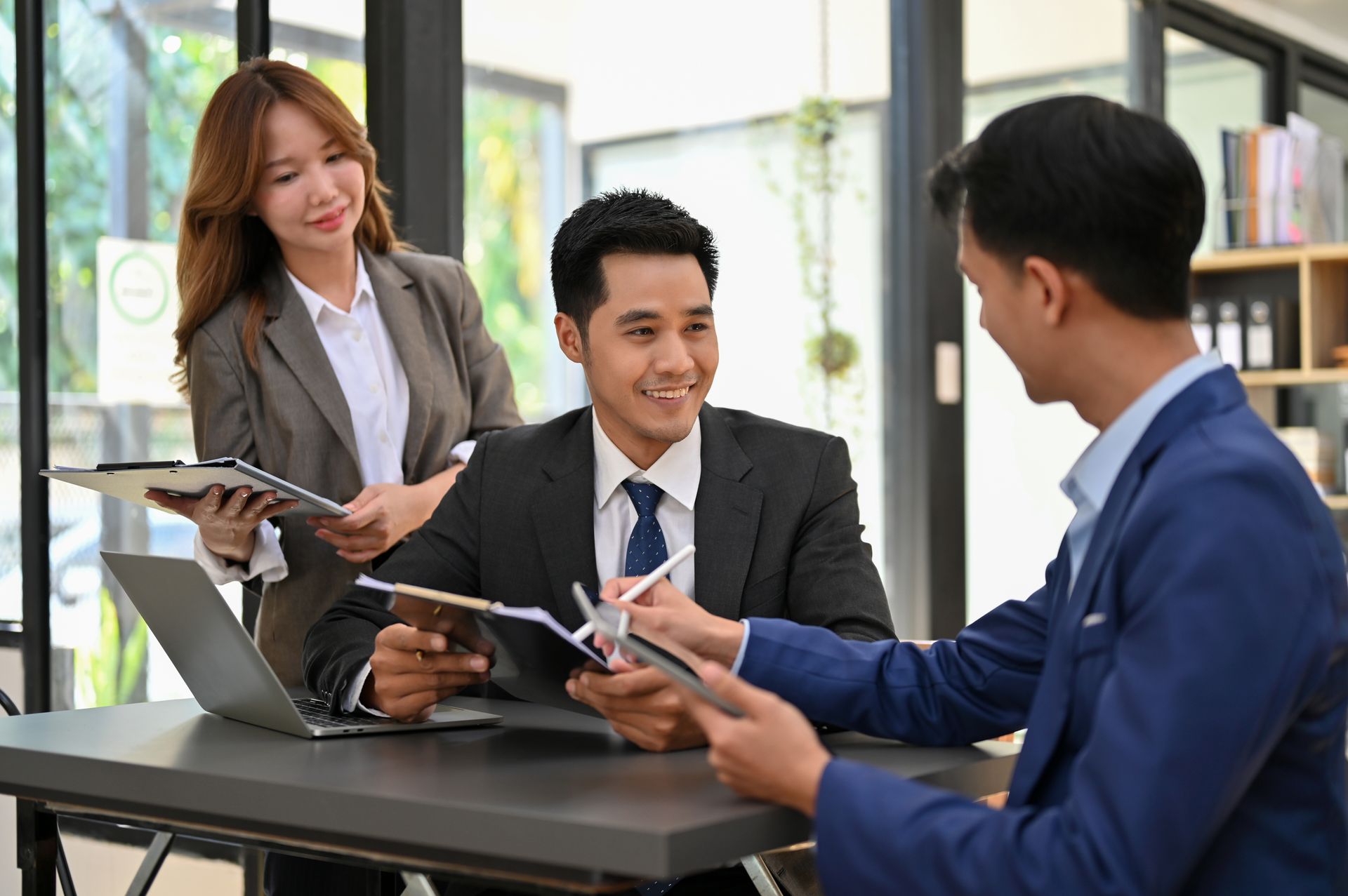 Three professionals reviewing documents and a laptop at an office table