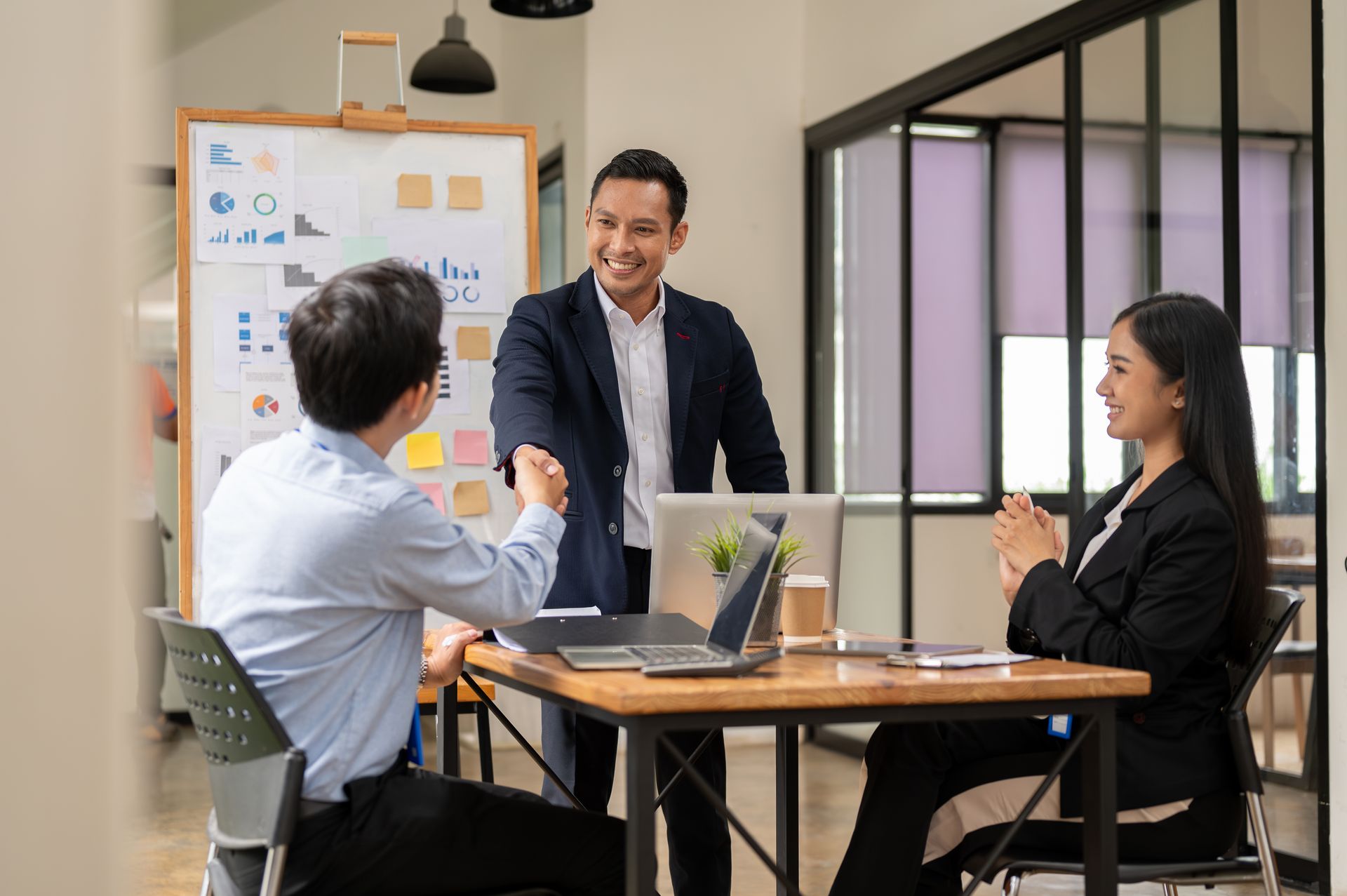 Three colleagues in business attire discussing at a table with a laptop