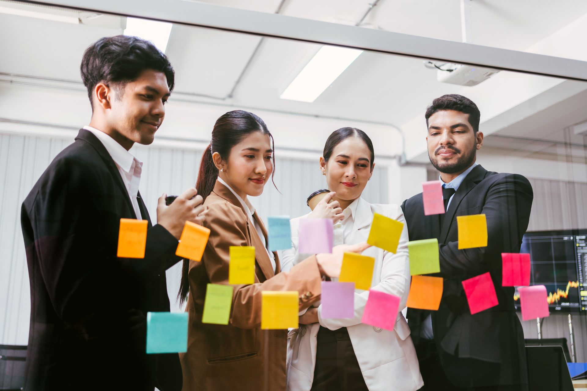 Four colleagues placing sticky notes on a glass wall during a brainstorm